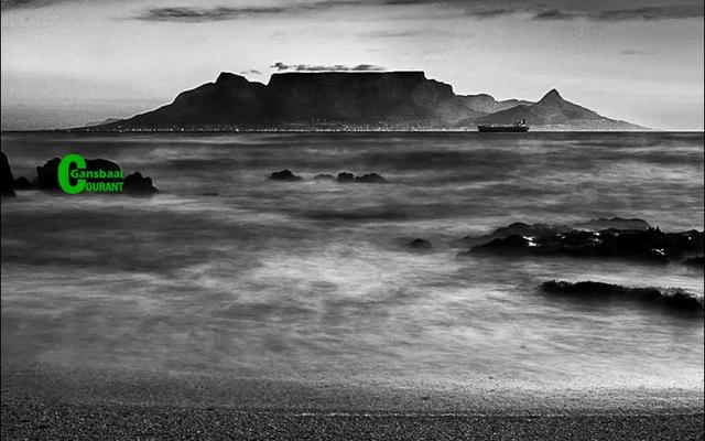 Nog ‘n besonderse foto deur Robert Johnson, Gansbaai Fotografieklub se opleidingsfotograaf, met ‘n wasige (blurred) oseaan op die voorgrond en ‘n duidelike beeld van Tafelberg en ‘n boot op die agtergrond. 
