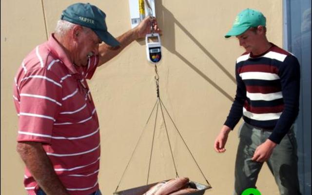 JP Uys (regs), wat die swaarste sak (6.75kg) in die Juniorkategorie ingeweeg het, beloer die wedstrydsekretaris, Jean Downing tydens die inweeg van sy vis.