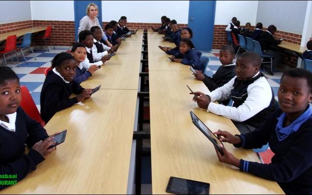 Leerders is hier druk besig om op tablette in die luukse rekenaarlokaal te werk. Hul opvoeder, Emeke Stieger staan links agter.