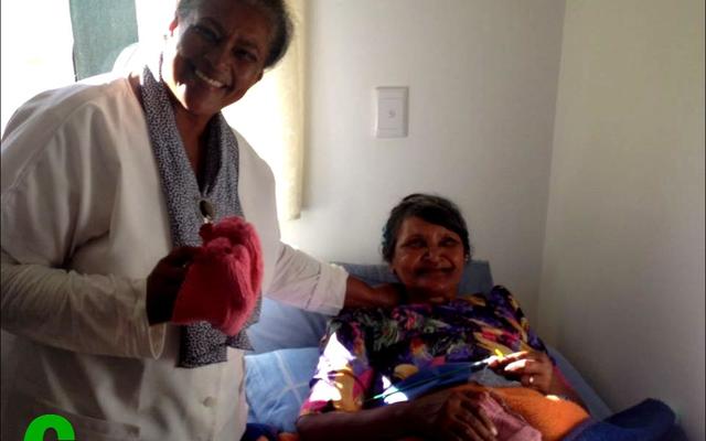 Francis Arends (links) van Oak Grove Nasorgsentrum staan by  Elizabeth Arendse se bed om sommer dadelik die geskenk-sokkies aan te trek.