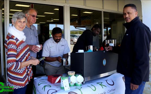 Die eienaars van Sunset Place Farm, Muriel en Chris Burls kry ‘n bietjie boeretroos van Xolani Soshweshwe van Miko en Puro Coffee.  Musa Noyni is baie besig op die agtergrond en Ashwell Gillion, vloerbestuurder by Overberg Agri, wag sy beurt af.